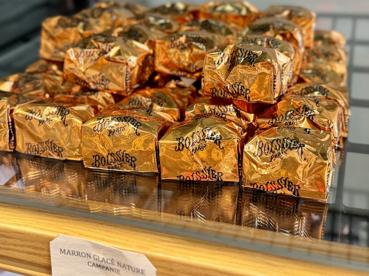a shelf of marrons glacés wrapped in golden paper in a Parisian shop